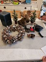 Overview of Canadiana Christmas collection items on table: pine wreath, ceramic moose head, two artificial pine trees, bird ornaments, and dark blue candle.