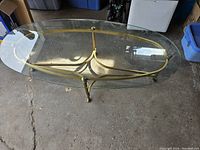 Oval coffee table showing entire top with glass surface and brass frame in light natural lighting on concrete floor.