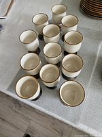 Top view of 12 beige ceramic goblets with rustic bases arranged on tablecloth.