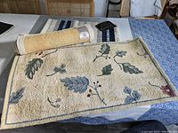 45x27 inch wool and cotton rug with leaf and berry design, rolled at one end, placed on a table