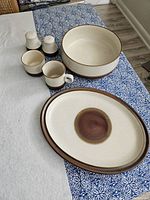 Full set arranged on a table, showing all six items: serving platter, salad bowl, salt and pepper shakers, cream server, and sugar bowl in a beige and rust red stoneware.