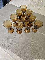10 amber wine glasses arranged in a triangular shape showing their amber tint and dark stems.