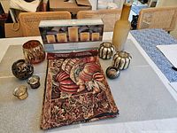 Overall view of the 14-piece autumn tableware collection arranged on a table including the tapestry table runner, candle holders, and a frosted glass bottle.