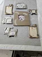Full set of 7 dog-themed photo frames laid out on a textile surface: metal frames with dog, bone, and doghouse motifs and one wooden cartoon dog face frame