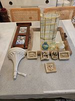 Photo showing 12 assorted decorative accent pieces on a table including an ornate white wall shelf bracket, wooden photo frame with hooks, glass display case, five small carved reliefs, three small glass decorative bottles, and a rustic wood piece.