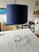 Full lamp assembled showing navy fabric shade and textured glass base on a white tablecloth.