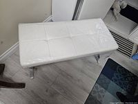 Top angled view of white leatherette bench showing tufted seat and chrome legs.