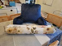 Blue reading pillow with quilted pattern and armrests on a table with a floral bolster pillow in front