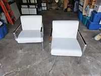 Pair of white leather and chrome Deco style reception chairs viewed from the front and slightly angled view in garage setting.