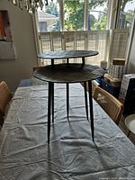 Pair of metal side tables displayed on a cloth-covered table under natural light, showing the taller table positioned behind the shorter table.