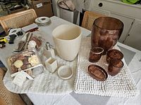 Photo shows collection of bathroom accessories including white containers, brown glass pieces, and decorative potpourri on table.