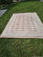 Full view of large wool Persian rug laid flat on grass outdoors showing geometric pattern and border design.