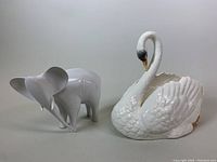 Photo showing both elephant and swan porcelain sculptures side by side on a plain background