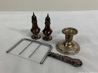 Four sterling silver pieces laid out on white surface: cheese cutter, candleholder, and salt and pepper shakers.