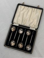 Six sterling silver spoons arranged in original vintage presentation box with black velvet insert and satin lid lining