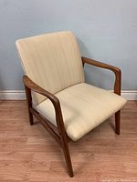 Side view showing the teak frame, armrests, and beige fabric upholstery with visible minor wear and fabric tear.