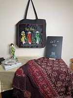 Full lot view showing all items including tote bag, throw blanket, plate and Geisha figurine on a table with lot plaque.