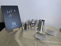 Two beer steins, lighter, and two small decorative metal trays on table with black easel board behind marking lot number.