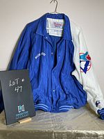 Front view of men's large Blue Jays shell jacket hanging on a hanger with the lot number card.