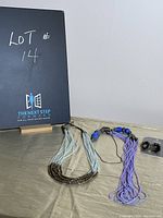 Two blue multi-strand necklaces and a pair of black bell-shaped earrings displayed on a surface with lot number board in background