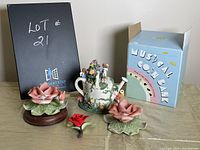 Overall lot photo showing three ceramic rose figurines and musical teapot coin bank with box.