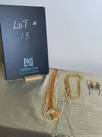 Photo of the costume jewelry lot including multi-strand necklace, gold necklace, and pair of earrings on a beige cloth surface with black stand showing lot number
