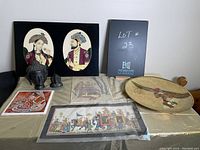 Full view of lot including framed prints, unframed prints, sculptures, and decorative plate on table.