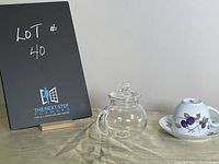 Photo showing the glass mini-teapot with lid and vintage Evesham England cup and saucer from a frontal angle on a beige surface.