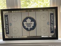 Full view of rectangular mirror with ice rink design and Toronto Maple Leafs logo at center, showing reflective surface and framing.
