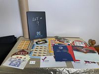 Wide view of large assortment of collected stamps and booklets on a table, including themed stamp sheets and commemorative materials.