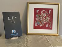 Framed Thai cloth painting on red background with traditional figure and gold frame, lot number card in the background