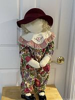 Full view of vintage Time Out Kid doll standing on wooden surface, dressed in floral romper and burgundy hat with curly blonde hair.