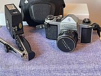 Vintage Asahi Pentax film camera with attached lens and lens cap, black leather case with embossed logo, and vintage detachable flash unit.