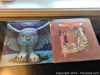 Two vinyl LP albums side by side: Rush 'Fly By Night' with a blue owl on the cover, Aerosmith 'Toys in the Attic' with various toys illustration on the cover.
