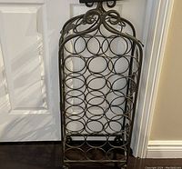 Front view of metal wine rack showing circular holders, floral and leaf design on top, and wheeled base.