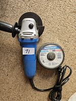 Blue handheld Mastercraft angle grinder with attached side handle, power cord coiled and secured with velcro strap. One cut-off wheel installed on the grinder and additional wheels placed beside it.