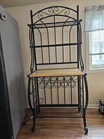 Front view of the black metal bakers rack with wood shelves and wine bottle holder section.