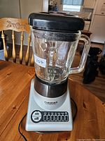 Front view of Cuisinart blender showing glass jar, black lid, silver base, and control buttons on wooden table.