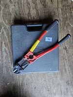 Bolt cutters placed on closed black molded case with handle and label partially visible.