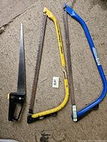 Three saws: two bow saws with blue and yellow frames each with 21-inch blades, and one handsaw with black handle, all showing signs of use and rust.