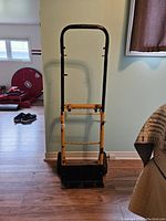 Front view of the yellow folding dolly standing upright showing the handle and platform.