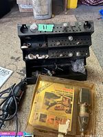 Photo of black perforated stand holding various Dremel rotary tool accessories and a black corded Dremel rotary tool on left. Yellow plastic accessories case labeled 'Dremel Mini Precision Rotary Tool' in package on lower right.