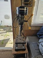 Front view of Mastercraft drill press mounted on a wooden table with wheels near sliding door.