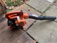 Side perspective showing orange engine housing, handle and black nozzle