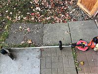 Full length view of orange and black Echo SRM-225 straight shaft trimmer laying on an outdoor mat and bricks with fallen leaves.