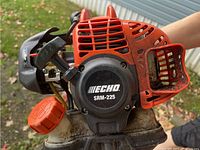 Close-up of engine housing with Echo SRM-225 label and black pull start cover, orange fuel cap visible below.