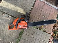 Full view of chainsaw on patio showing bar, chain, handles and body