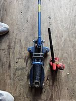 Top view of two jacks side by side on wooden floor, blue trolley jack and red bottle jack.