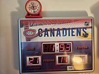 Front view of large Montreal Canadiens digital clock with red LED display showing time, temperature, period, and month, with small analog clock placed on top.