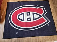 Photo of rectangular rug on wooden floor showing Montreal Canadiens logo in red, white, and black.